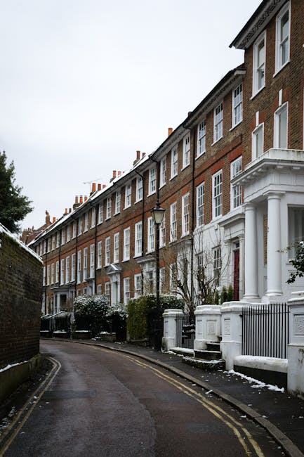 A narrow residential street in Muswell Hill featuring a row of terraced brick houses with white window frames, some with front gardens enclosed by white-painted railings and steps leading up to the do